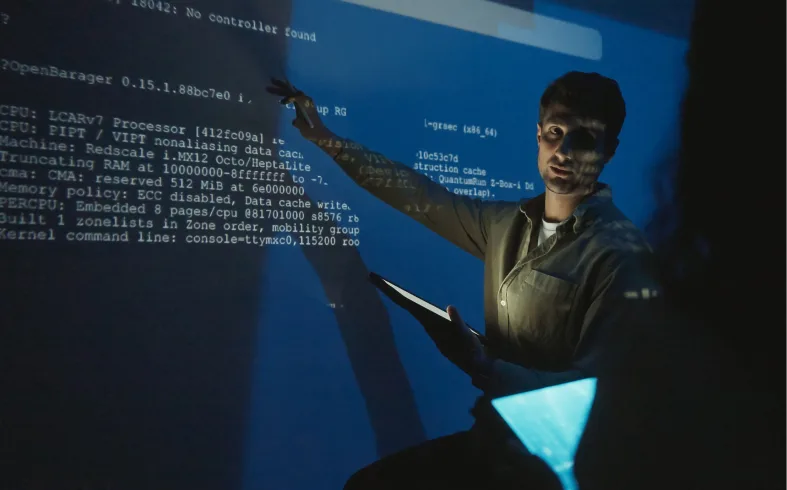 Person pointing at code projected on a screen in a dark room.