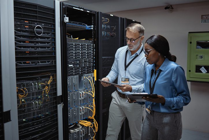 Two IT professionals working in a server room, managing network equipment.