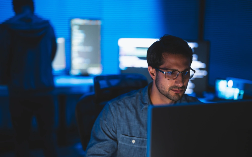 Man working late on a computer in a dark office.