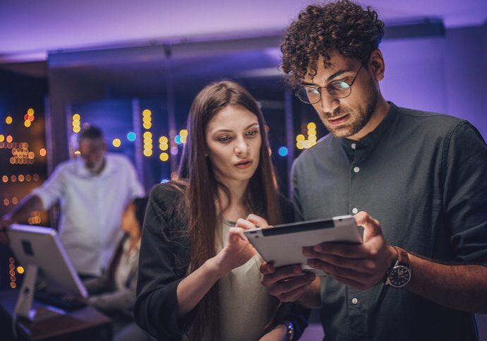 Two young adults intently looking at a tablet in a modern indoor setting.