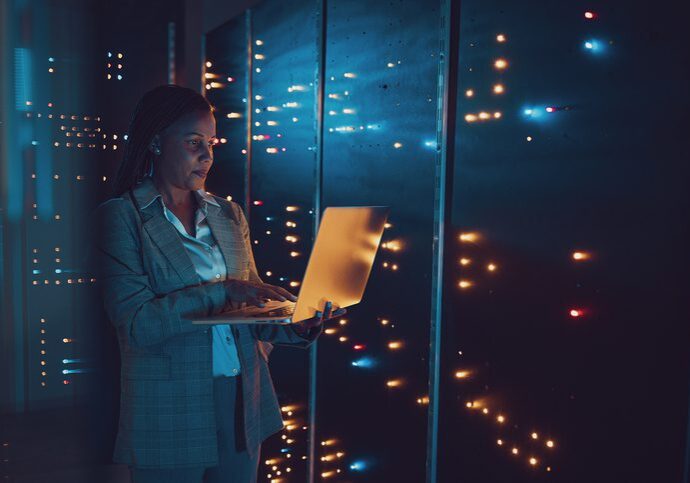 Woman working on laptop in an office at night with city lights outside.