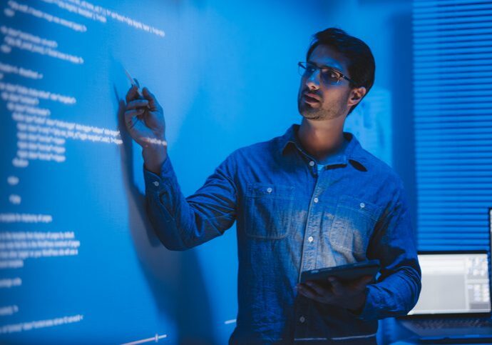 Man writing or drawing on a transparent board with blue light.